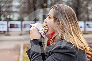 Young hungry woman eats Burger and takes lunch break outdoors in Park.Fast food. Takeaway food concept