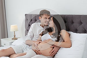 Young husband and his pregnant wife lying in bed