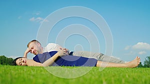 Young husband with his pregnant wife relaxing in the park, together lie on the green grass