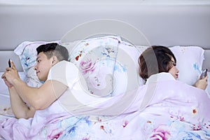 Young husband and wife lying on bed with cellphone