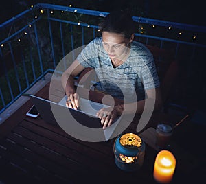 Young hysster woman working on a laptop in the evening on the open terrace of her country house, cozy with candles and lanterns