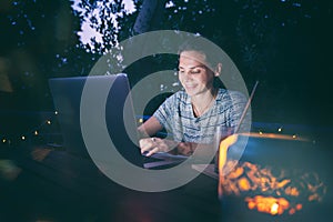 Young hysster woman working on a laptop in the evening on the open terrace of her country house, cozy with candles and lanterns