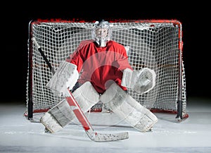 A young ice-hockey goaltender in a ready position against a dark photo