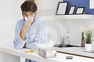 Young ill man blowing nose in tissue paper