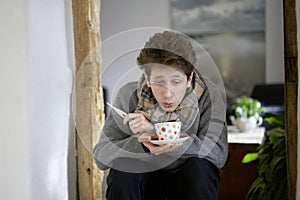 Young ill man sitting in his home with a cup of tea and a thermometer in his hands