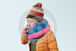 Young ill man in winter hat and scarf coughing being sick.