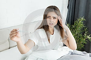 Young ill woman sitting in bed holding termometer in her hands feeling sick early in the morning photo