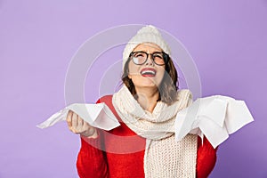 Young ill woman wearing winter hat isolated over purple background holding napkin
