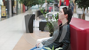 A young impatient woman is sitting on a sofa and holding a protective mask at her hands, in the waiting room, looking around. Side