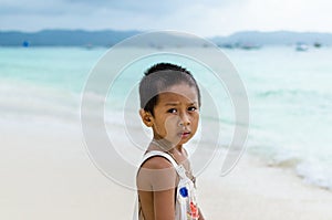 Young impoverished asian boy at white beach on Boracay
