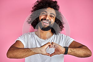 Young indian or arabic man smiling in love doing heart symbol shape with hands