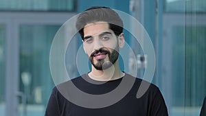 Young Indian Arabic student or businessman with mustache and beard looks affably into camera outdoors. Smiling middle