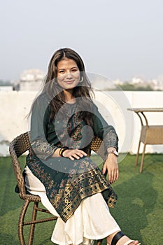 Young indian beautiful girl posing towards the camera, while sitting on the chair. Girl wearing indian traditional dress