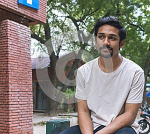 A young indian boy with french cut mustache sitting idle