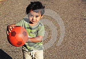 A Young Indian boy playing with a red ball