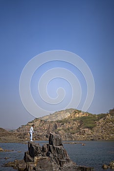 Young indian boy standing on a cliff near a landscape of a lake and mountain in the background