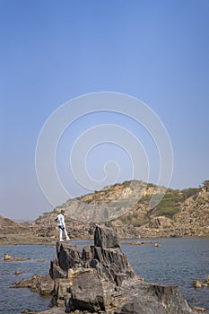 Young indian boy standing on a cliff near a landscape of a lake and mountain in the background