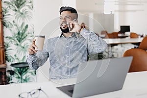 Young indian business male on laptop and coffee in modern office