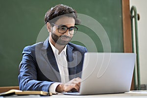 Young indian business man in suit working on laptop computer sitting in office.