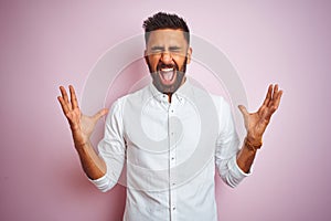 Young indian businessman wearing elegant shirt standing over isolated pink background celebrating mad and crazy for success with