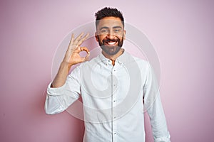 Young indian businessman wearing elegant shirt standing over isolated pink background smiling positive doing ok sign with hand and