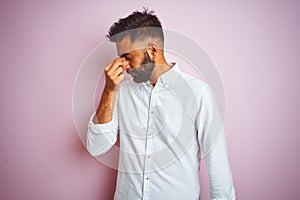 Young indian businessman wearing elegant shirt standing over isolated pink background tired rubbing nose and eyes feeling fatigue