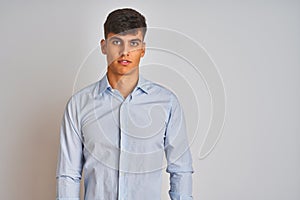 Young indian businessman wearing elegant shirt standing over isolated white background with serious expression on face