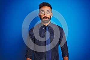 Young indian businessman wearing elegant shirt and tie standing over isolated blue background puffing cheeks with funny face
