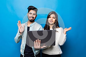 Young indian couple greeting on video call while standing with laptop isolated on blue background