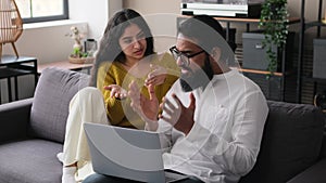 Young Indian Couple With Laptop Disputing While Sitting On Sofa