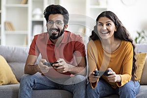 Young Indian Couple Playing Video Games With Joysticks At Home