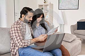 Young indian couple reading bills paying online using laptop at home.