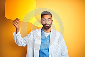 Young indian doctor man holding speech bubble standing over isolated yellow background with a confident expression on smart face