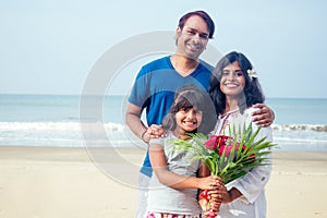 Young indian family relaxing at the beach on beautiful summer day in Goa with bouquet of roses