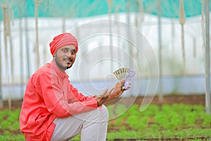 young indian farmer counting and showing money at greenhouse or polyhouse