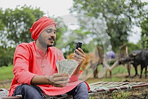 Young indian farmer showing money and talking on mobile phone at home