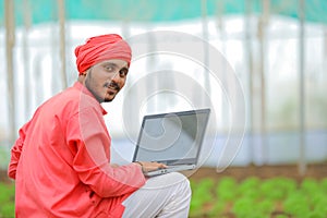 Young indian farmer using laptop at greenhouse or polyhouse