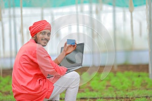 Young indian farmer using laptop at greenhouse or polyhouse