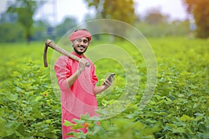 Young indian farmer using smartphone in green cotton field