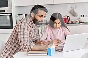 Young indian father helping school child teen daughter studying online at home.