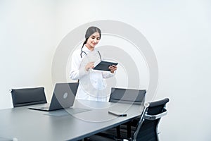 Young Indian female doctor wearing a white lab coat and stethoscope, standing by the table