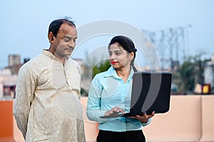 Young indian female in formal dress with laptop showing something to a middle aged man on internet, She is teaching computer and