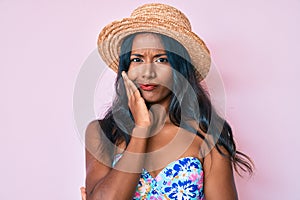 Young indian girl wearing bikini and summer hat thinking looking tired and bored with depression problems with crossed arms
