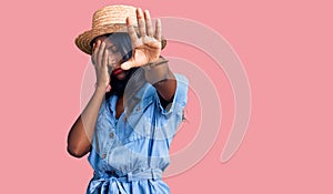 Young indian girl wearing summer hat covering eyes with hands and doing stop gesture with sad and fear expression