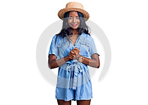 Young indian girl wearing summer hat with hands together and crossed fingers smiling relaxed and cheerful