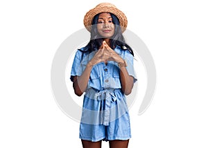 Young indian girl wearing summer hat hands together and fingers crossed smiling relaxed and cheerful