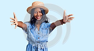 Young indian girl wearing summer hat looking at the camera smiling with open arms for hug