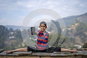 Young indian kid showing his mobile phone while doing a yoga pose