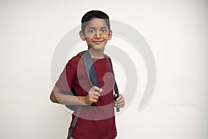 Young indian kid standing on a white wall with a school bag on his back. Getting ready for school. School and education concept