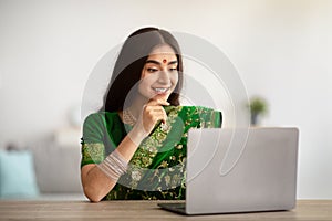 Young Indian lady in beautiful sari dress studying or working online on laptop, indoors